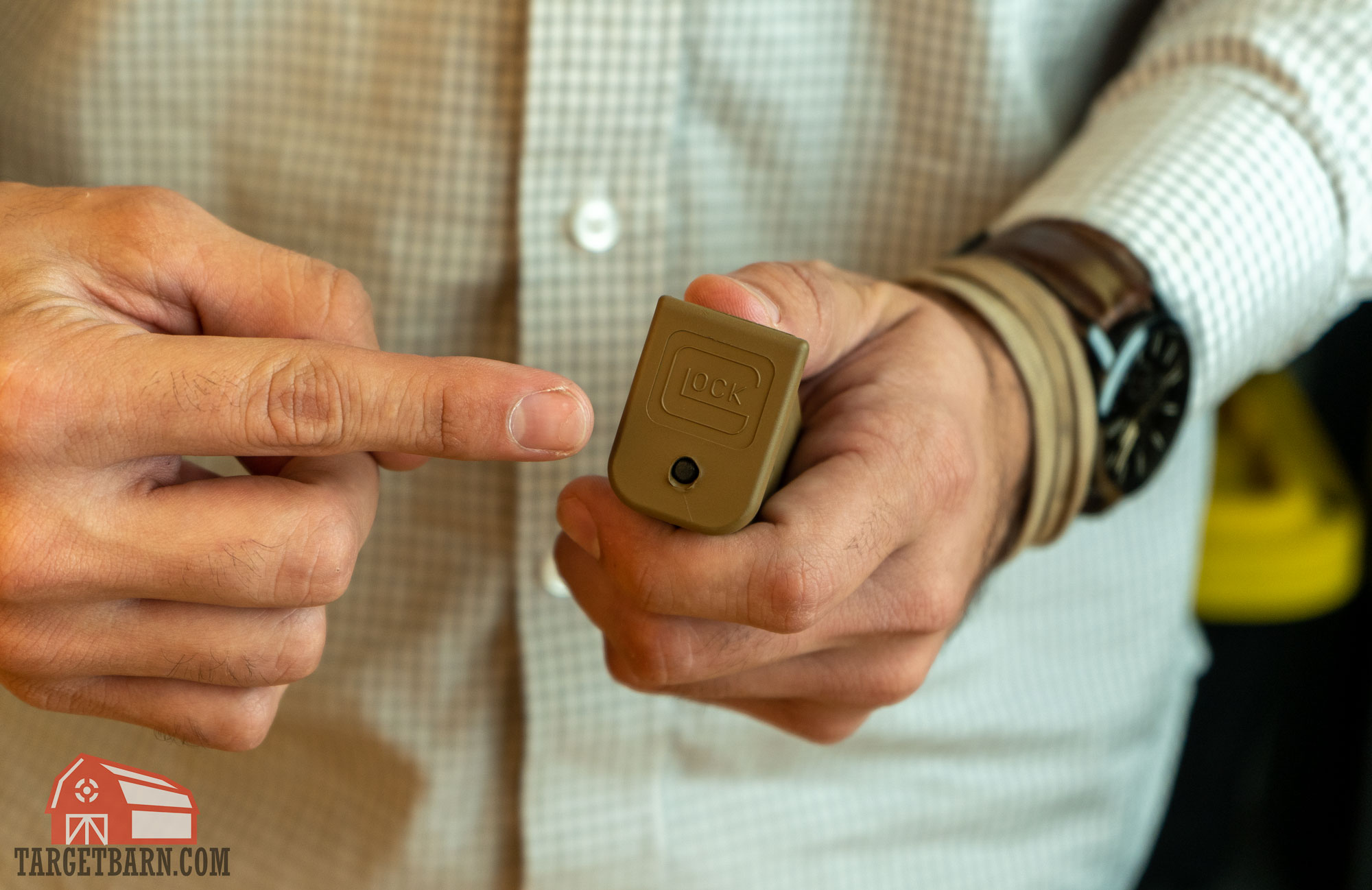 a man holding a glock magazine, pointing to the hole on the magazine floor plate