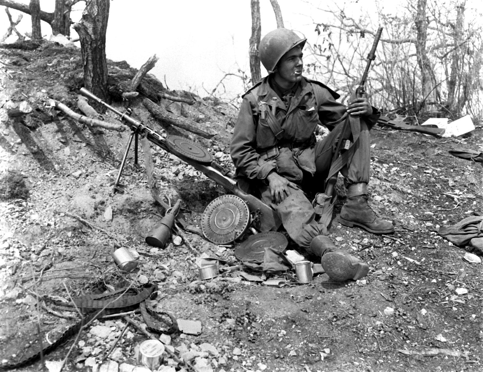 a black and white image of a u.s. army soldier with m1 carbine and soviet DP light machine gun sitting on a hill during the korean war