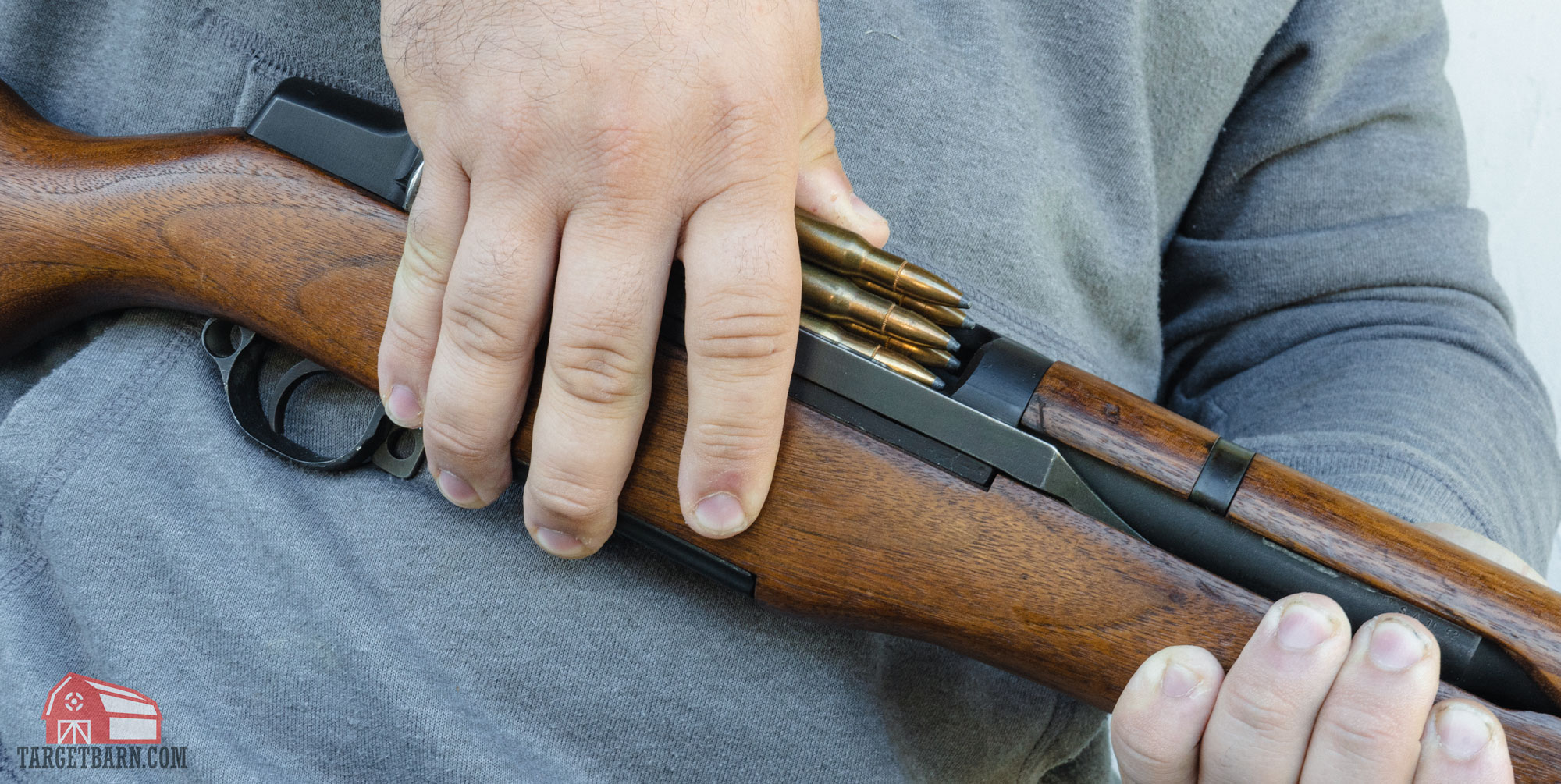 a man loading an en bloc clip with .30-06 ammo into an m1 garand rifle