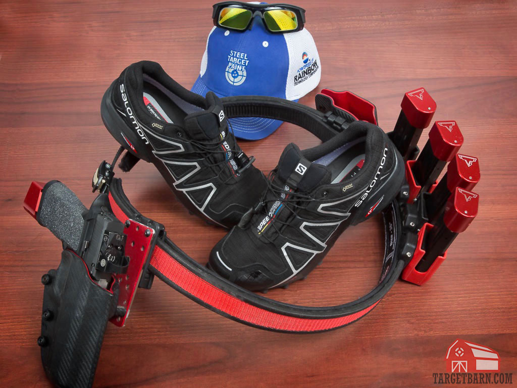 a competition gun and belt, salomon shoes, a hat, and protective eyewear displayed to demonstrate gear needed for a uspsa match