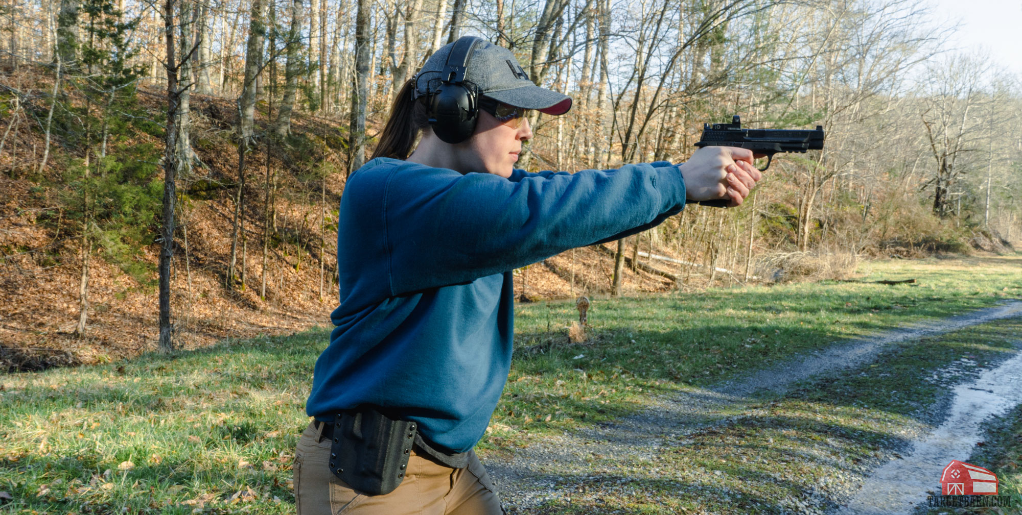the author shooting a pistol at an outdoor range wearing proper range clothes including a hat, eye protection, ear protection and a high-cut shirt